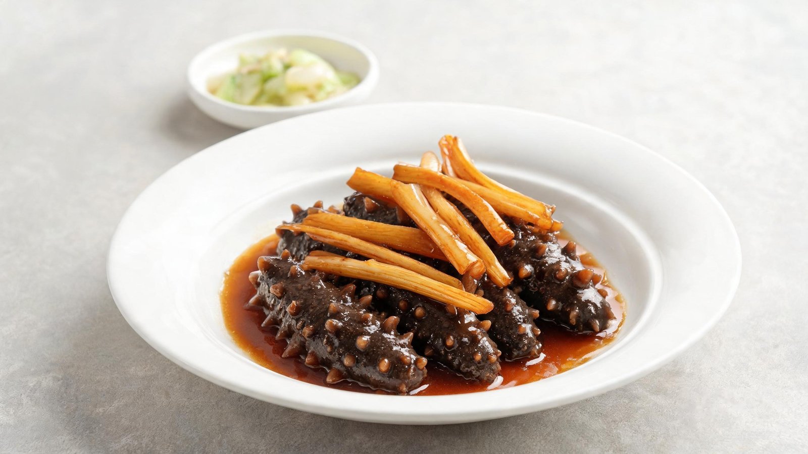 Braised sea cucumber with scallions in glossy brown sauce on a white plate